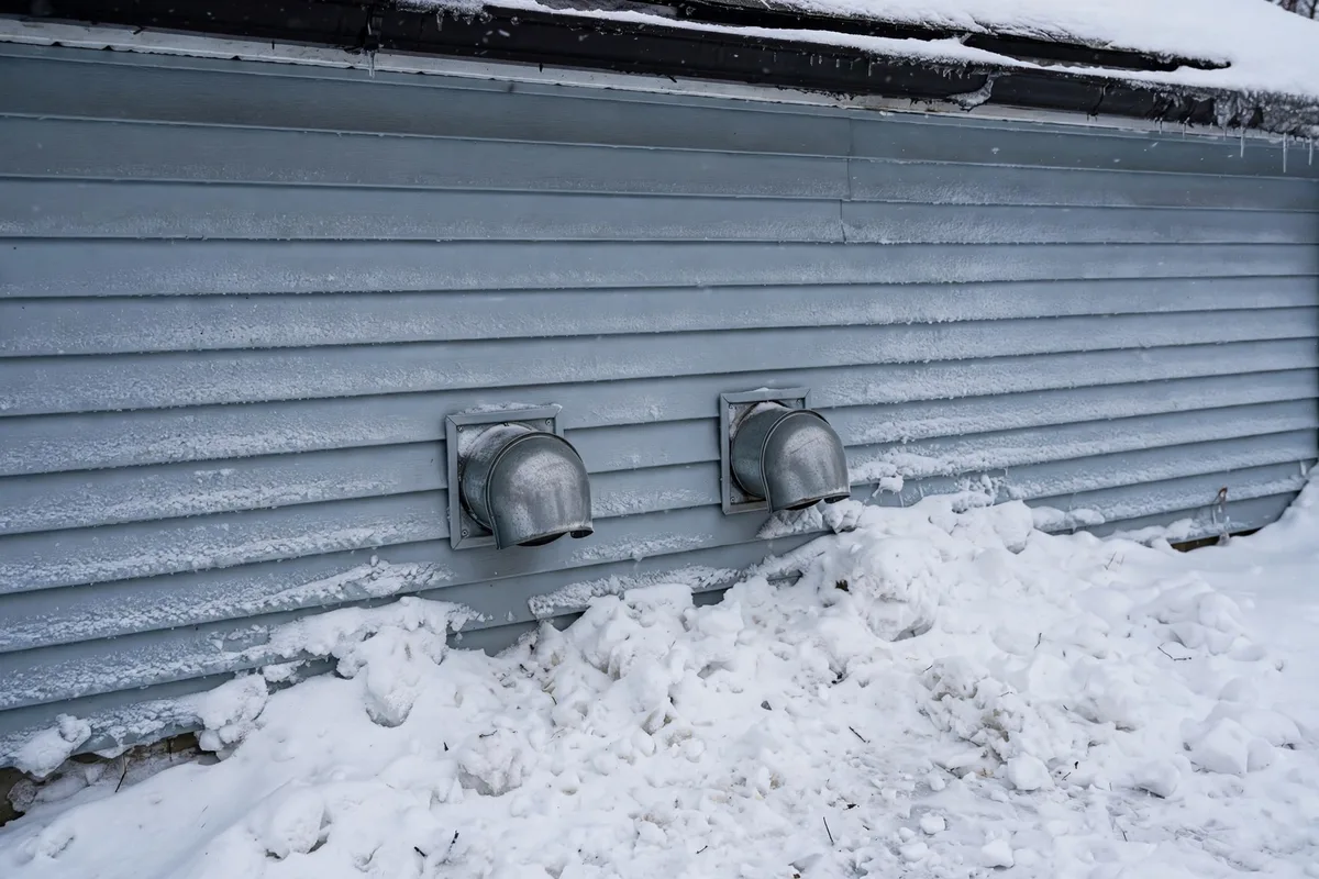 Two furnace vent pipes on a snowy house wall in Laramie